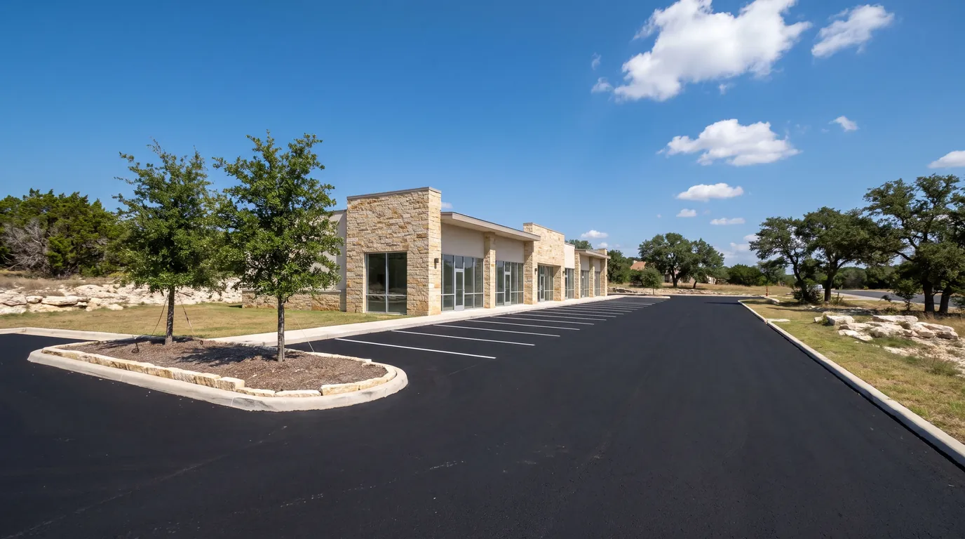 Fresh white parking stall lines on a newly paved lot in front of a small limestone retail strip